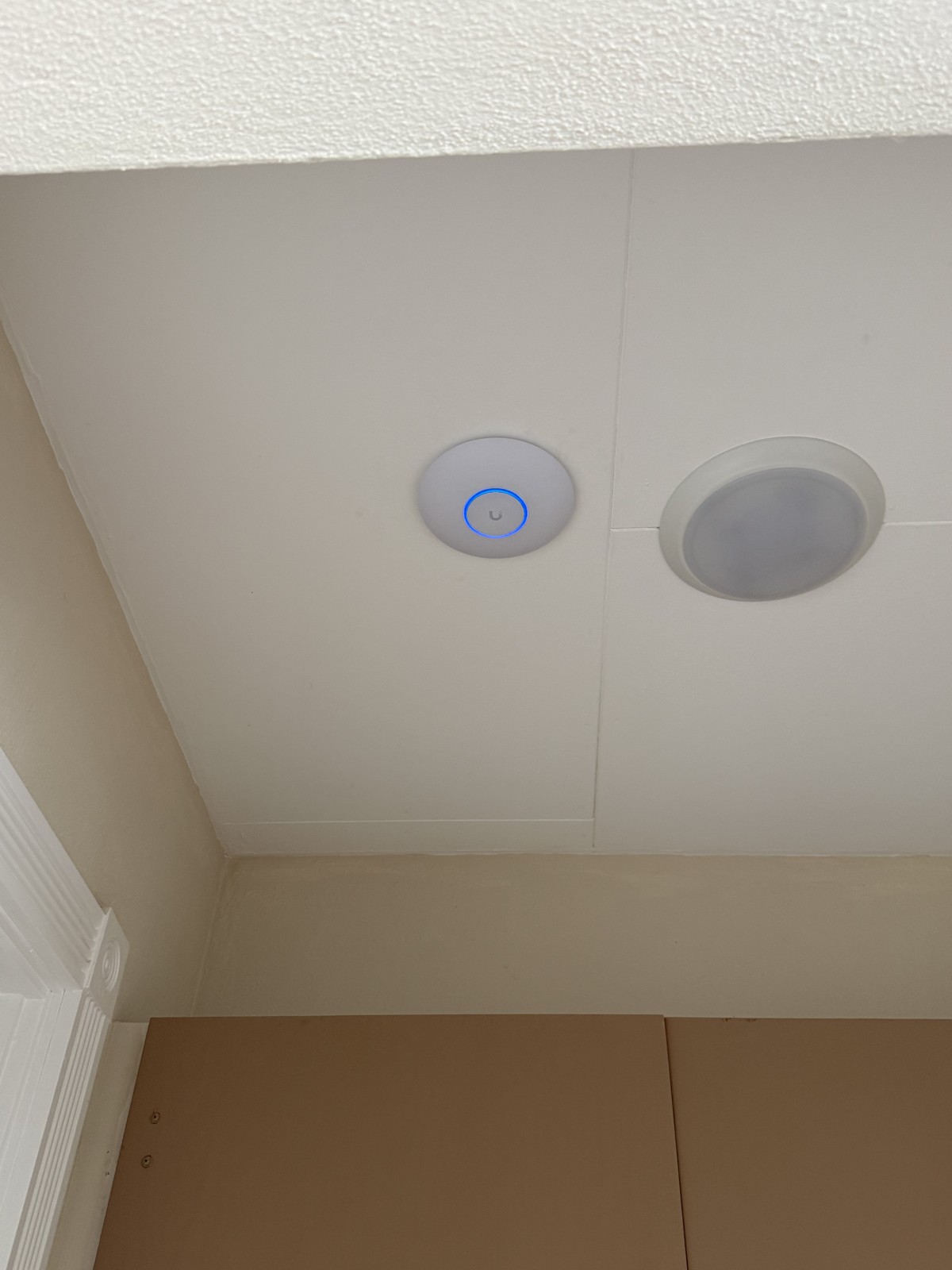 UniFi ceiling access point beside a recessed light